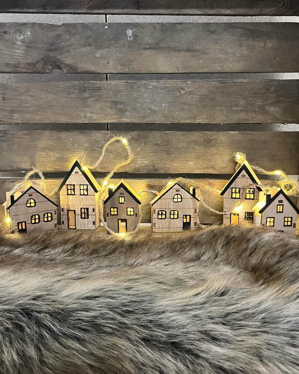 Lichterkette Homewood mit sechs Holzhäusern auf Fellunterlage, ideal für gemütliche Raumdekoration.