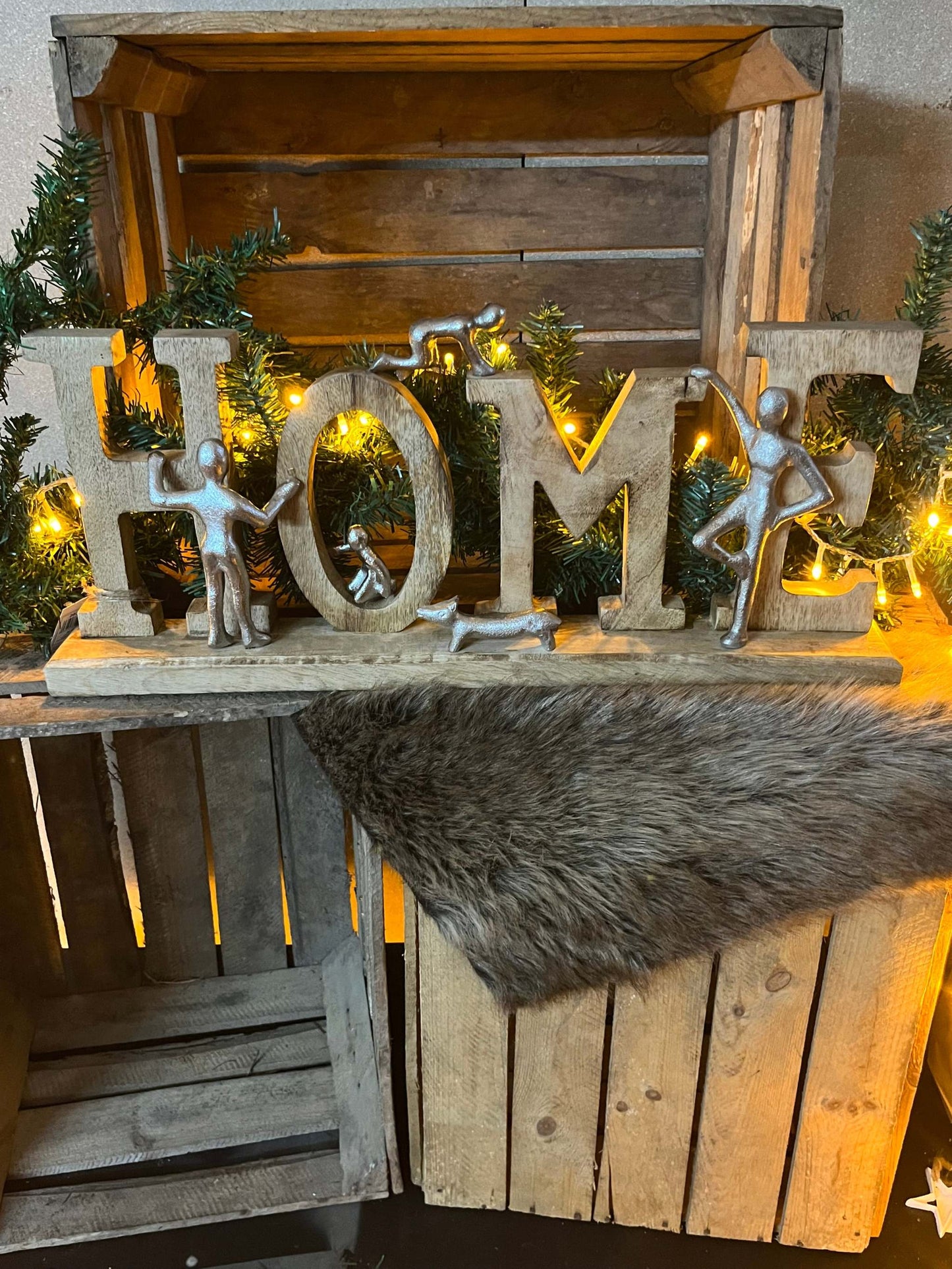 Schriftzug "Home" aus Mangoholz und Aluminium, dekorativ auf Holzkisten mit Lichterkette und Tannenzweigen, ca. 26 cm hoch.